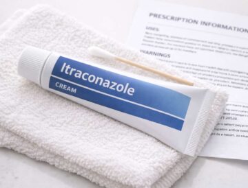 Tube of itraconazole cream and cotton swab on a clean towel next to a prescription leaflet.